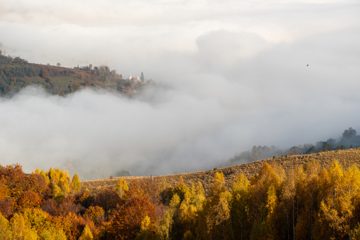 View of a church nestled in a valley surrounded by dense fog and vibrant autumn foliage on the hillsides in Alba Iulia Alba County Romania. View of a church nestled in a valley surrounded by dense fog and vibrant autumn foliage on the hillsides in Alba Iulia Alba County Romania.