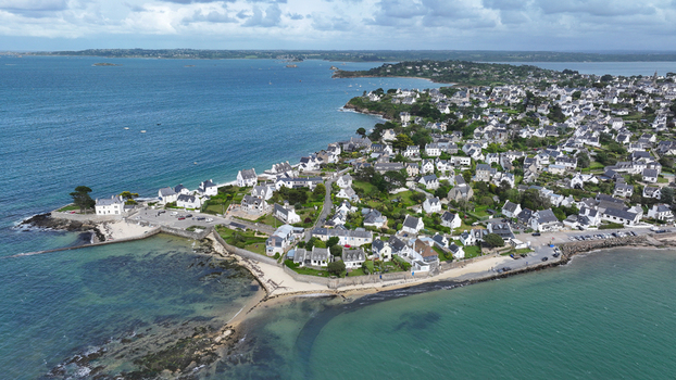 Aerial view of the coastal town featuring white houses with grey roofs sandy beaches and turquoise sea water in Carantec Brittany France. Aerial view of the coastal town featuring white houses with grey roofs sandy beaches and turquoise sea water in Carantec Brittany France.