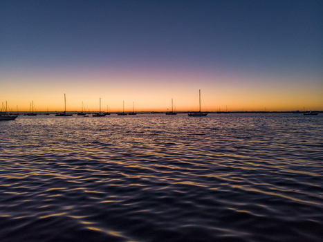Aerial view of sailboats anchored in the bay at sunset near the Malecon de La Paz with calm rippling water reflecting the orange and purple sky in La Paz Baja California Sur Mexico.