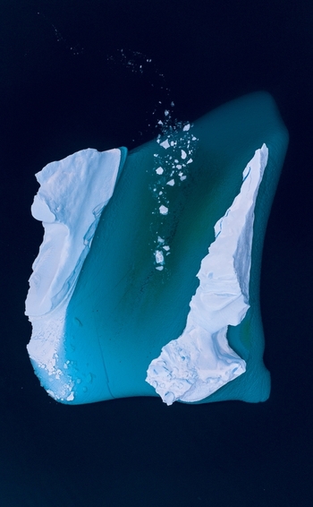 Aerial view of a large iceberg floating in dark blue arctic waters with a visible turquoise underwater shelf and small ice fragments Tasiilaq Sermersooq Municipality Greenland. Aerial view of a large iceberg floating in dark blue arctic waters with a visible turquoise underwater shelf and small ice fragments Tasiilaq Sermersooq Municipality Greenland.