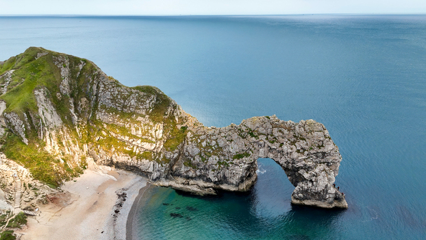 Aerial view of Durdle Door a natural limestone arch on the Jurassic Coast with its rocky cliffs sandy beach and clear blue sea in Wareham England United Kingdom. Aerial view of Durdle Door a natural limestone arch on the Jurassic Coast with its rocky cliffs sandy beach and clear blue sea in Wareham England United Kingdom.