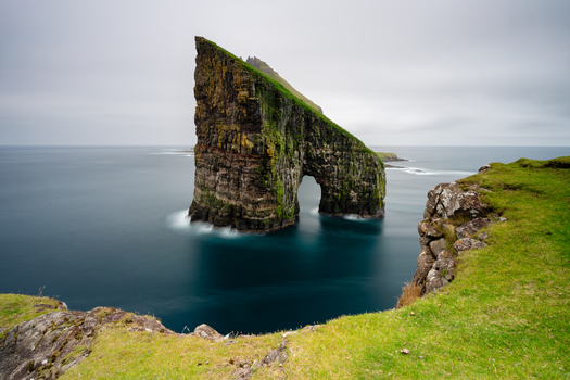 View of Drangarnir sea arch with mossy cliffs and calm ocean waters Faroe Islands.
