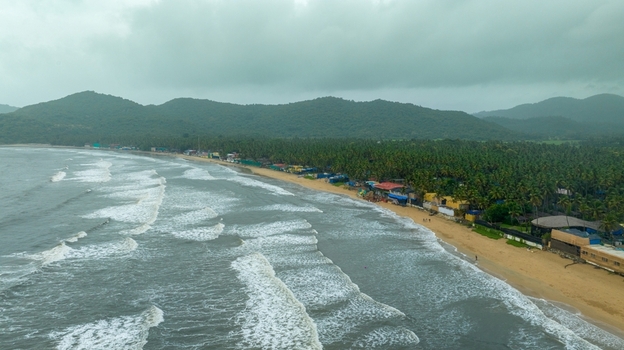 Aerial view of Palolem Beach with sandy coastline lush palm trees rolling waves and green hills in Canacona Goa India.