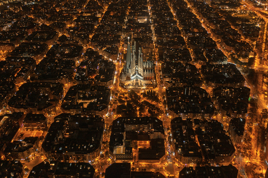 Aerial view of the illuminated Sagrada Familia basilica at night surrounded by the dense grid of city blocks and glowing street lights in Barcelona Catalonia Spain. Aerial view of the illuminated Sagrada Familia basilica at night surrounded by the dense grid of city blocks and glowing street lights in Barcelona Catalonia Spain.
