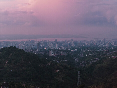 Aerial view of Busay hills overlooking the urban skyline and coastal landscape under a purple sunset sky in Cebu City Central Visayas Philippines.