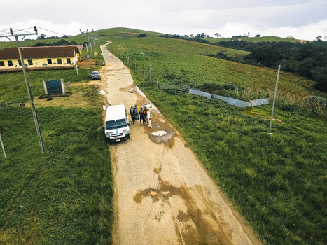 Aerial view of a white van and people on a muddy road with rolling green hills and a brown roofed building under an overcast sky Obudu Cross River Nigeria.