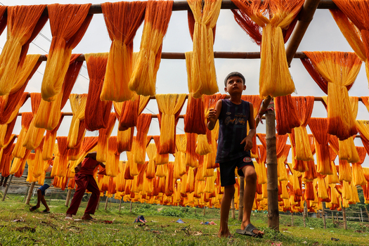 Narayanganj Bangladesh 29 March 2026 View of vibrant sun drenched threads cascading like fiery waterfalls a young boy amidst the dyed yarns a scene of industrious artistry. Narayanganj Bangladesh 29 March 2026 View of vibrant sun drenched threads cascading like fiery waterfalls a young boy amidst the dyed yarns a scene of industrious artistry.