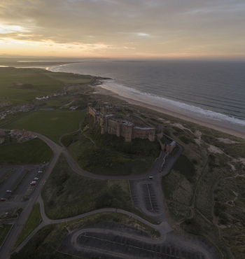 Aerial view of Bamburgh Castle overlooking the sandy beach and North Sea at sunset in Bamburgh England United Kingdom. Aerial view of Bamburgh Castle overlooking the sandy beach and North Sea at sunset in Bamburgh England United Kingdom.