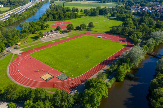 Aerial view of Sport Island Forchheim featuring a red running track and green fields surrounded by trees and the Regnitz river in Forchheim Bavaria Germany. Aerial view of Sport Island Forchheim featuring a red running track and green fields surrounded by trees and the Regnitz river in Forchheim Bavaria Germany.