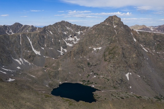 Aerial view of the rugged Mount of the Holy Cross in the Sawatch Range with a dark alpine lake nestled in the rocky basin under a blue sky in Vail Colorado United States. Aerial view of the rugged Mount of the Holy Cross in the Sawatch Range with a dark alpine lake nestled in the rocky basin under a blue sky in Vail Colorado United States.