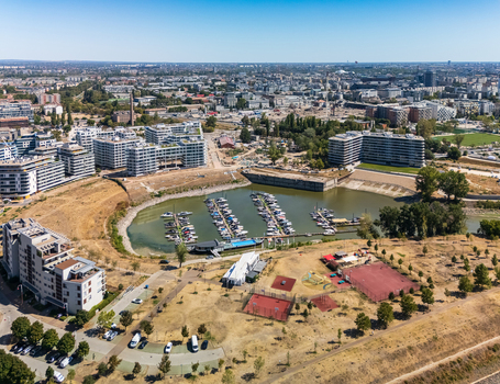 Aerial view of a marina with moored boats beside modern apartment complexes construction sites and recreational courts in Budapest Hungary showing waterfront urban redevelopment. Aerial view of a marina with moored boats beside modern apartment complexes construction sites and recreational courts in Budapest Hungary showing waterfront urban redevelopment.
