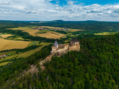 Aerial view of Tocnik Castle perched on a forested hill surrounded by rolling agricultural fields and meadows under a cloudy blue sky in Tocnik Stredocesky kraj Czechia. Aerial view of Tocnik Castle perched on a forested hill surrounded by rolling agricultural fields and meadows under a cloudy blue sky in Tocnik Stredocesky kraj Czechia.