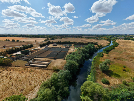 Aerial view of a wastewater treatment works situated next to a river surrounded by fields and trees under a blue sky with scattered clouds in St Neots England United Kingdom. Aerial view of a wastewater treatment works situated next to a river surrounded by fields and trees under a blue sky with scattered clouds in St Neots England United Kingdom.