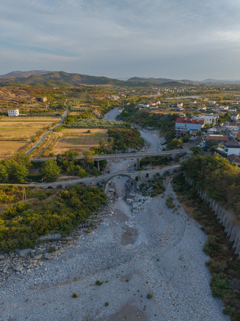 Aerial view of Mesi Bridge spanning the dry riverbed with surrounding rural landscape stone arches and distant hills in Boks Qarku i Shkodres Albania.