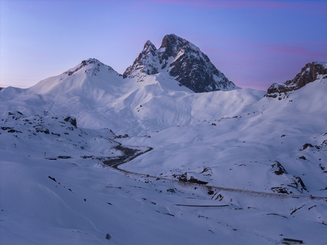 Aerial view of the snow covered Pyrenees mountains with a winding road cutting through the landscape under a soft twilight sky in Spain. Aerial view of the snow covered Pyrenees mountains with a winding road cutting through the landscape under a soft twilight sky in Spain.