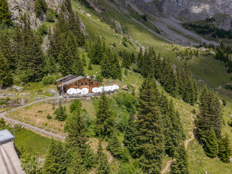 Aerial view of Tallihutte SAC mountain hut nestled among pine trees and lush green slopes in the Swiss Alps Innertkirchen Bern Switzerland.