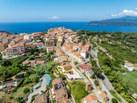 Aerial view of the historic town of Capoliveri featuring terracotta roofed buildings winding streets and lush greenery overlooking the blue Mediterranean Sea in Capoliveri Tuscany Italy.
