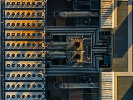 Aerial view of an industrial plant rooftop featuring rows of cooling fans and complex pipe systems under golden hour light in Rome Lazio Italy.