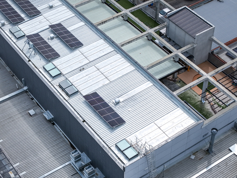 Aerial view of solar panels installed on a corrugated metal roof of an industrial building with skylights and concrete structural beams in Melbourne VIC Australia.