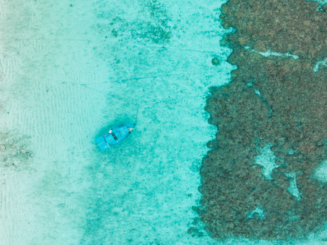 Aerial view of a lone turquoise boat floating in the crystal clear shallow waters near a dark reef Vashafaru Island Maldives. Aerial view of a lone turquoise boat floating in the crystal clear shallow waters near a dark reef Vashafaru Island Maldives.
