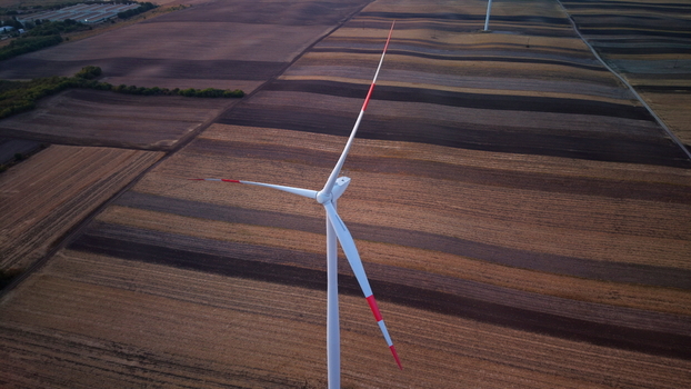 Aerial view of a wind turbine standing in a vast agricultural field with striped patterns of tilled soil in Vladimirovac Vojvodina Serbia. Aerial view of a wind turbine standing in a vast agricultural field with striped patterns of tilled soil in Vladimirovac Vojvodina Serbia.