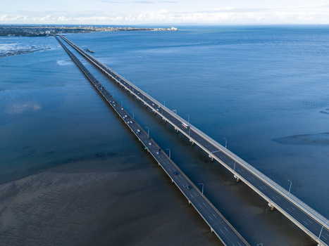 Aerial view of the Ted Smout Memorial Bridge spanning across the calm blue waters of Bramble Bay with vehicles on the road and shallow sandbanks visible in Brighton Queensland Australia. Aerial view of the Ted Smout Memorial Bridge spanning across the calm blue waters of Bramble Bay with vehicles on the road and shallow sandbanks visible in Brighton Queensland Australia.