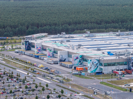 Aerial view of Tesla Gigafactory Berlin Brandenburg with industrial building solar panels colorful murals loading docks trucks and parking lot in Grunheide Mark Brandenburg Germany. Aerial view of Tesla Gigafactory Berlin Brandenburg with industrial building solar panels colorful murals loading docks trucks and parking lot in Grunheide Mark Brandenburg Germany.