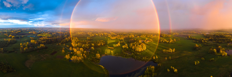 Aerial view of a circular rainbow over the lush green fields forests and a small pond in the rural landscape of Latvia. Aerial view of a circular rainbow over the lush green fields forests and a small pond in the rural landscape of Latvia.