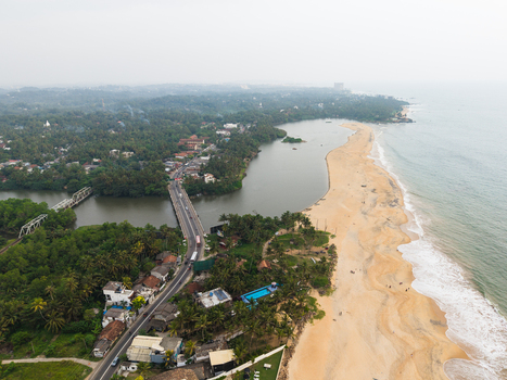 Aerial view of a sandy beach coastline with a bridge crossing a river and dense tropical greenery in Galle Southern Province Sri Lanka.