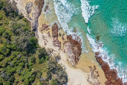 Aerial view of North Stradbroke Island coastline featuring turquoise ocean waves sandy beach rocky outcrops and lush coastal vegetation in Redland City Queensland Australia. Aerial view of North Stradbroke Island coastline featuring turquoise ocean waves sandy beach rocky outcrops and lush coastal vegetation in Redland City Queensland Australia.