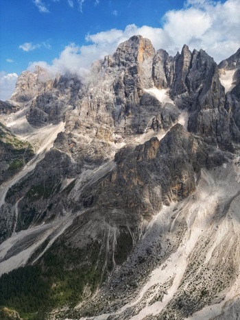 Aerial view of the jagged peaks of the Dolomite Mountains with rocky slopes and white clouds under a blue sky in Canazei Trentino South Tyrol Italy. Aerial view of the jagged peaks of the Dolomite Mountains with rocky slopes and white clouds under a blue sky in Canazei Trentino South Tyrol Italy.