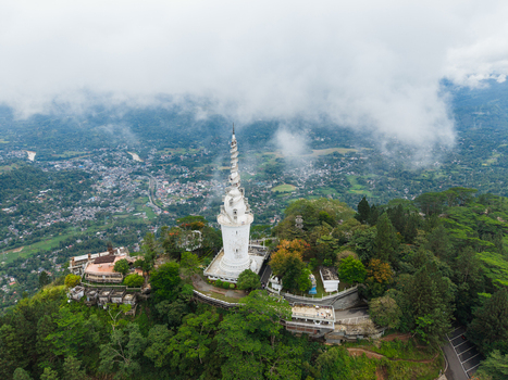 Aerial view of the white spiral Ambuluwawa Tower on a lush hilltop surrounded by misty clouds and green forest overlooking the town Gampola Central Province Sri Lanka. Aerial view of the white spiral Ambuluwawa Tower on a lush hilltop surrounded by misty clouds and green forest overlooking the town Gampola Central Province Sri Lanka.
