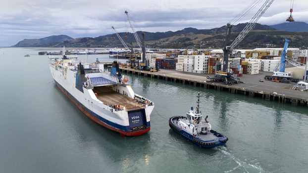 Nelson New Zealand 19 February 2026 Aerial view of Port Nelson with a large cargo ship being assisted by a tugboat near industrial cranes and shipping containers. Nelson New Zealand 19 February 2026 Aerial view of Port Nelson with a large cargo ship being assisted by a tugboat near industrial cranes and shipping containers.