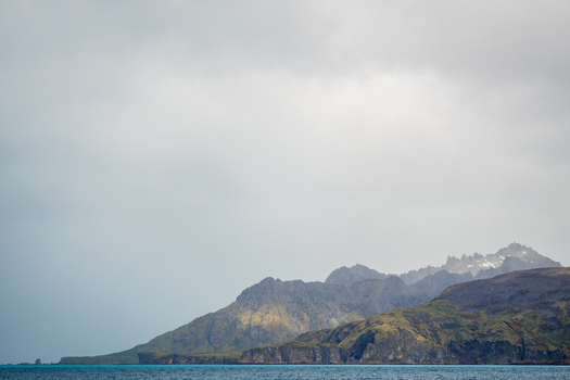View of the rugged coastline and dramatic mountain peaks under a cloudy sky South Georgia and the South Sandwich Islands.