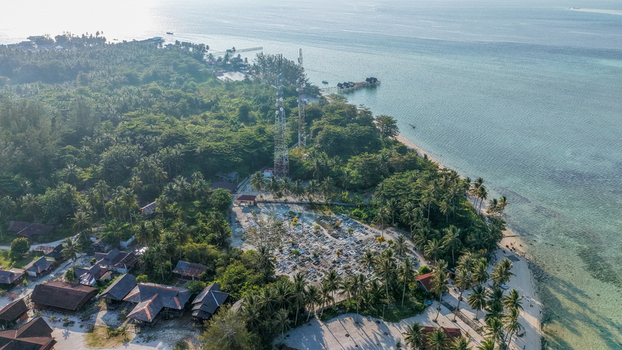 Aerial view of Pulau Derawan featuring a dense cemetery surrounded by tropical trees wooden houses and turquoise waters along the coastline in Pulau Derawan East Kalimantan Indonesia. Aerial view of Pulau Derawan featuring a dense cemetery surrounded by tropical trees wooden houses and turquoise waters along the coastline in Pulau Derawan East Kalimantan Indonesia.
