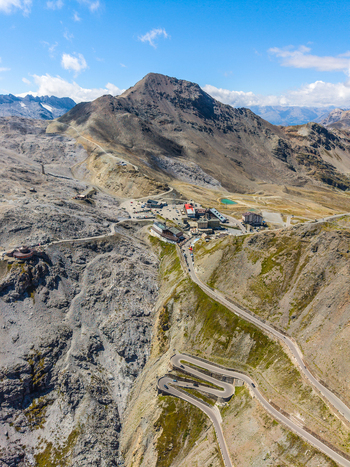 Aerial view of the winding Stelvio Pass road with hairpin turns surrounded by rugged mountain peaks and rocky alpine terrain under a clear blue sky in Stilfs Trentino Alto Adige Italy.
