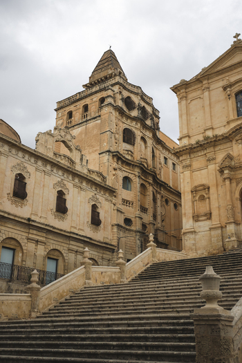 View of the grand stone staircase leading to the ornate baroque facade of Noto Cathedral under a cloudy sky in Noto Sicily Italy. View of the grand stone staircase leading to the ornate baroque facade of Noto Cathedral under a cloudy sky in Noto Sicily Italy.