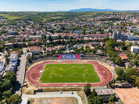 Aerial view of Eger stadium with a football pitch running track and grandstands surrounded by residential neighborhoods trees and rolling hills in Hungary on a summer day. Aerial view of Eger stadium with a football pitch running track and grandstands surrounded by residential neighborhoods trees and rolling hills in Hungary on a summer day.