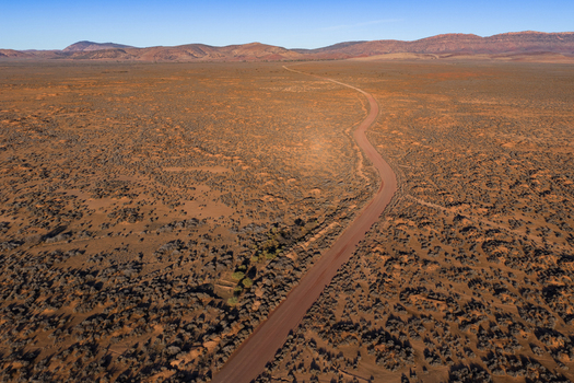 Aerial view of a winding dirt road stretching through the vast arid landscape and rugged mountain ranges under a clear blue sky in Flinders Ranges South Australia Australia. Aerial view of a winding dirt road stretching through the vast arid landscape and rugged mountain ranges under a clear blue sky in Flinders Ranges South Australia Australia.
