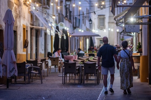 Evora Portugal 08 September 2026 View of a couple walking hand in hand along a historic street lined with outdoor restaurant seating and illuminated by string lights at dusk. Evora Portugal 08 September 2026 View of a couple walking hand in hand along a historic street lined with outdoor restaurant seating and illuminated by string lights at dusk.
