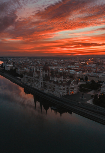 Aerial view of the Hungarian Parliament Building reflected in the Danube River under a vibrant orange sunset sky in Budapest Hungary.