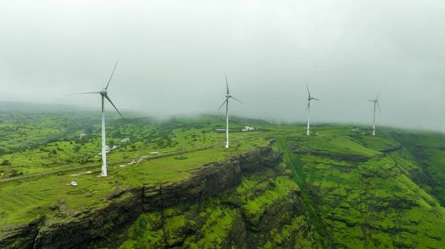 Aerial view of wind turbines standing on a lush green cliffside in the misty Western Ghats near Igatpuri Maharashtra India. Aerial view of wind turbines standing on a lush green cliffside in the misty Western Ghats near Igatpuri Maharashtra India.