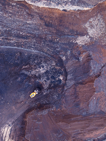 Aerial view of a yellow mining truck operating in a vast open pit mine with dark textured earth and deep excavation layers in Iceland. Aerial view of a yellow mining truck operating in a vast open pit mine with dark textured earth and deep excavation layers in Iceland.