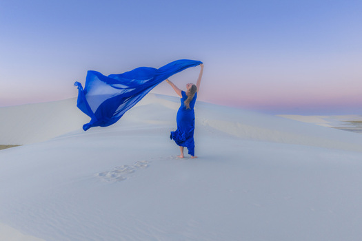 Aerial view of a woman in a blue dress holding a flowing fabric on the white sand dunes of Parque Nacional dos Lencois Maranhenses under a soft pastel sky Lencois Maranhenses MA Brazil. Aerial view of a woman in a blue dress holding a flowing fabric on the white sand dunes of Parque Nacional dos Lencois Maranhenses under a soft pastel sky Lencois Maranhenses MA Brazil.