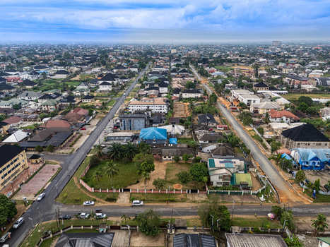 Aerial view of a sprawling urban landscape crisscrossed by grey roads dotted with diverse buildings and vibrant green spaces under an expansive cloudy sky Uyo Akwa Ibom Nigeria. Aerial view of a sprawling urban landscape crisscrossed by grey roads dotted with diverse buildings and vibrant green spaces under an expansive cloudy sky Uyo Akwa Ibom Nigeria.