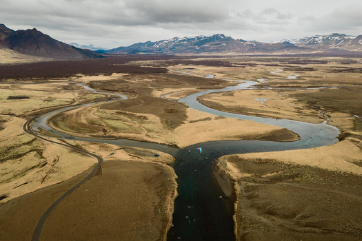 Aerial view of a winding river flowing through the vast barren landscape with a paraglider soaring above the water and distant mountains in Borgarbyggd Iceland. Aerial view of a winding river flowing through the vast barren landscape with a paraglider soaring above the water and distant mountains in Borgarbyggd Iceland.