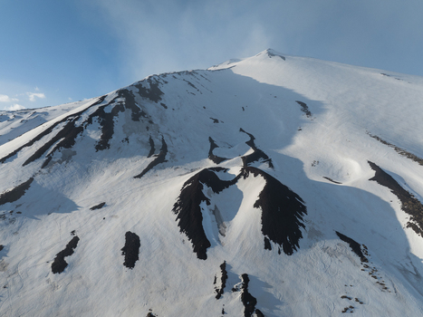 Aerial view of the snow covered south slope of Mount Etna featuring volcanic craters and dark lava patches under a clear blue sky in Nicolosi Sicilia Italy. Aerial view of the snow covered south slope of Mount Etna featuring volcanic craters and dark lava patches under a clear blue sky in Nicolosi Sicilia Italy.