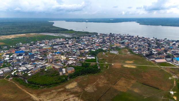 Aerial view of the coastal town of Minima featuring dense residential housing winding roads and lush green vegetation bordering the river estuary in Minima Rivers Nigeria.