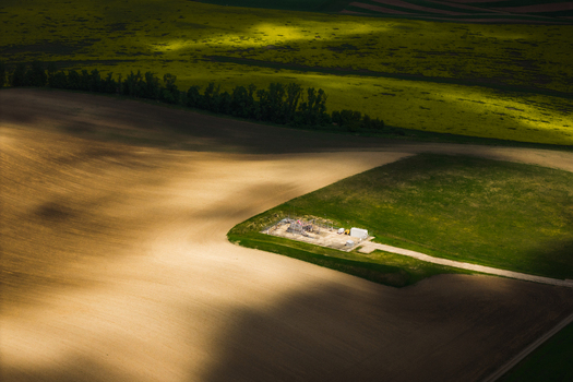 Aerial view of agricultural fields with a small industrial facility surrounded by green and brown soil under shifting cloud shadows in Brno South Moravian Region Czechia.