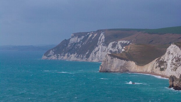 Aerial view of the dramatic white chalk cliffs of Lulworth Cove with turquoise sea waves crashing against the rugged coastline in Wareham England United Kingdom. Aerial view of the dramatic white chalk cliffs of Lulworth Cove with turquoise sea waves crashing against the rugged coastline in Wareham England United Kingdom.